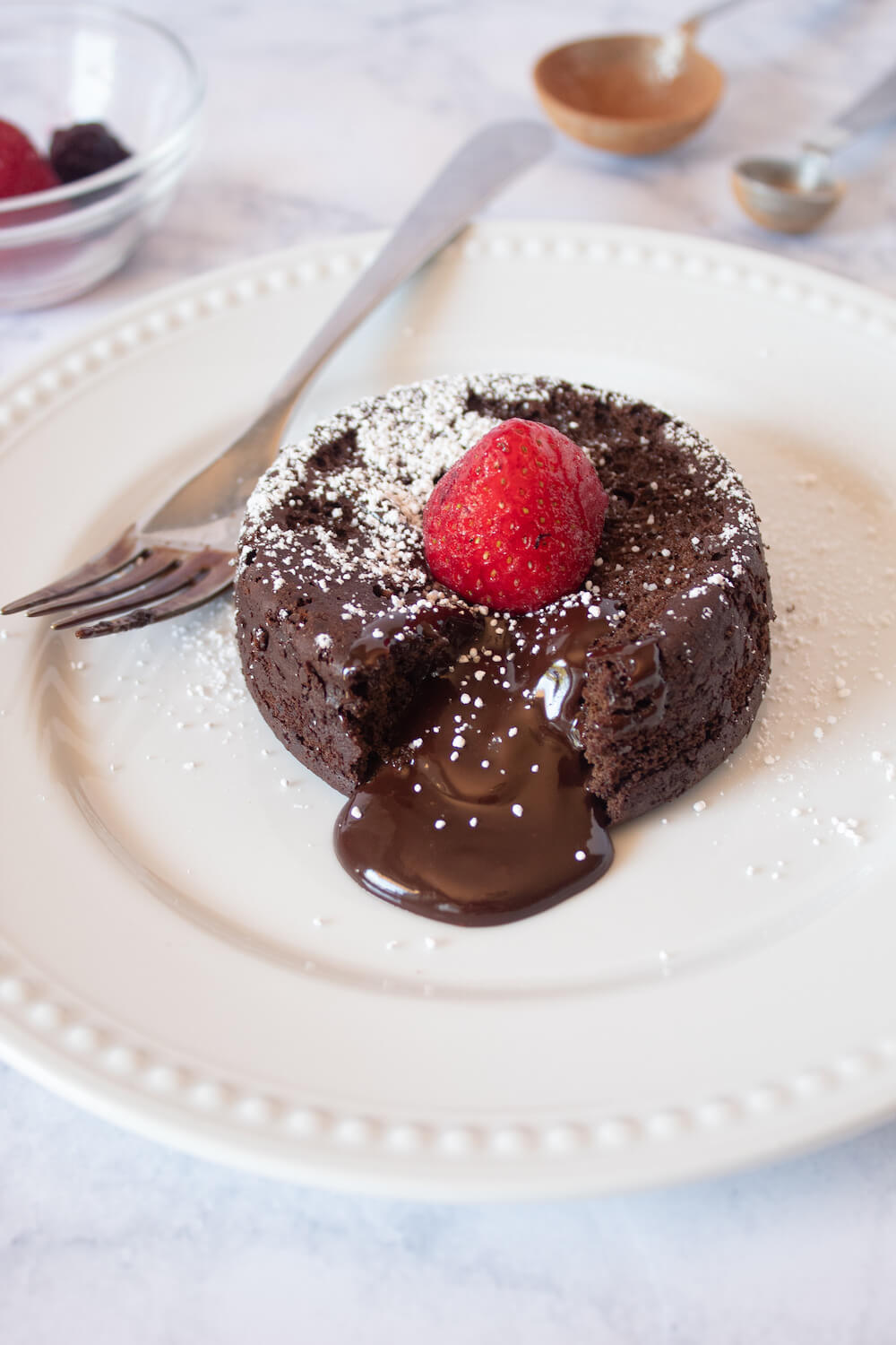 Keto Lava Cake dessert recipe served on a white plate with a fresh strawberry on top.