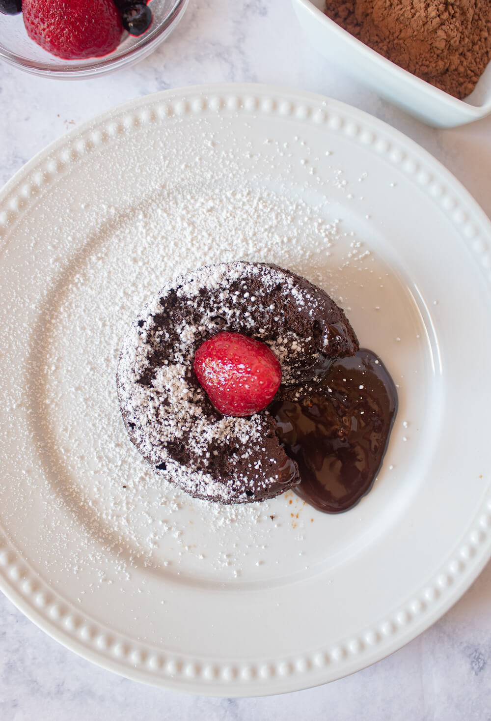 Overhead photo of Keto lava cake on white plate with gooey chocolate lava coming out.