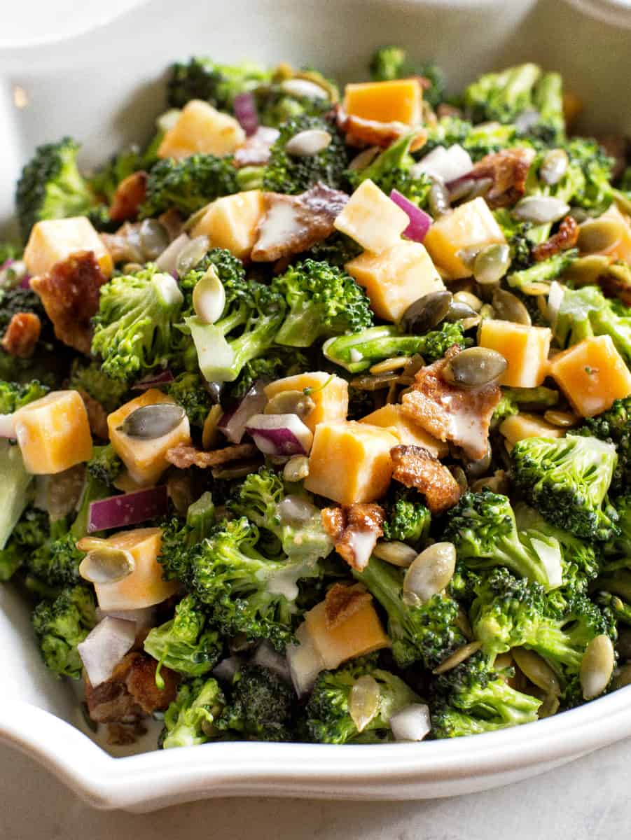 An image showcasing a Keto Broccoli Salad - a colorful, appetizing salad made up of fresh, vibrant green broccoli florets, crispy bacon pieces, shredded cheese, finely chopped onion, and a sprinkling of crunchy sunflower and pumpkin seeds. These ingredients are tossed in a creamy and tangy mayonnaise dressing, creating a beautiful contrast of colors and textures. This salad is served in a bowl, signifying its role as a perfect low-carb, keto-friendly side dish.